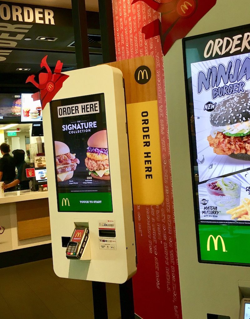 A self-order kiosk at a McDonald's in Singapore. The franchise offers a Ninja Burger fried chicken sandwich, among other destination-specific items. / Skift Table
