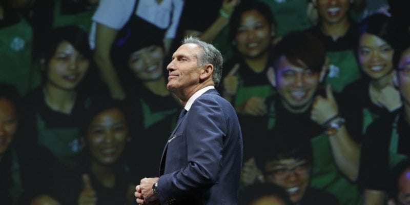 Starbucks CEO Howard Schultz walks in front of a photo of Starbucks baristas, at the coffee company's annual shareholders meeting in Seattle. Starbucks Corp. says Schultz is stepping down executive chairman later this month. - Ted S. Warren / Associated Press