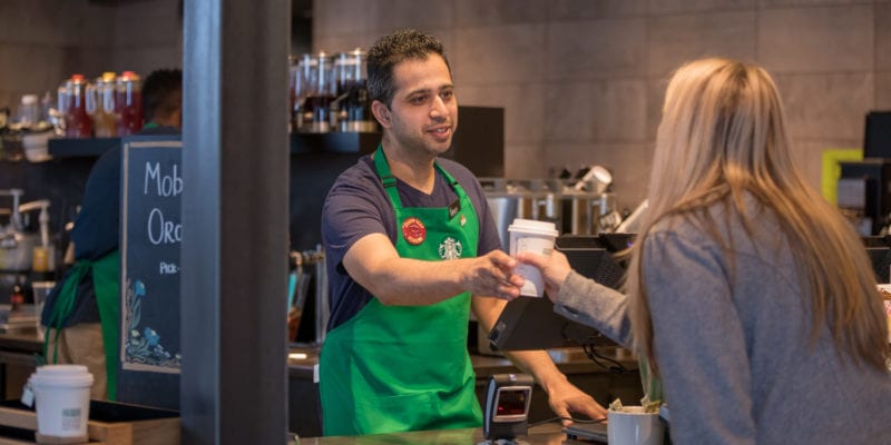 Starbucks barista hands customer her prepared coffee. / Bloomberg